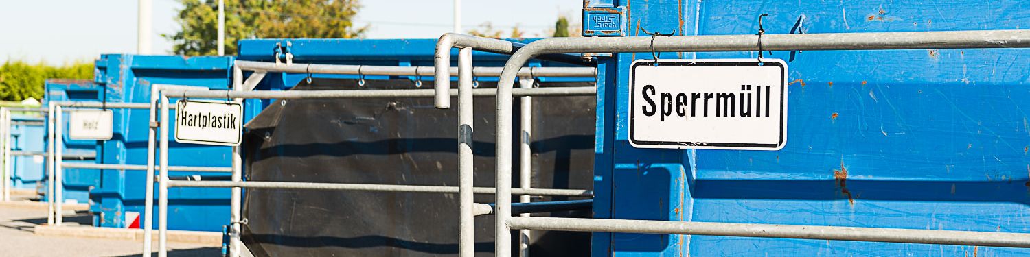 Drei blaue Container auf dem Wertstoffhof mit den Schildern "Sperrmüll", "Hartplastik" und "Holz"